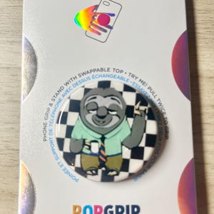 May include: A PopSockets PopGrip featuring a cartoon sloth wearing a shirt and tie, set against a black and white checkered background. The packaging includes the PopSockets and PopGrip logos, and text that reads "Phone Grip & Stand with Swappable Top."