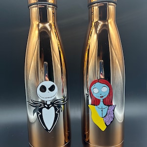Op de afbeelding: Twee roestvrijstalen waterflessen in ros&eacute;-goud met een Nightmare Before Christmas-thema. De ene fles heeft Jack Skellington en de andere Sally.