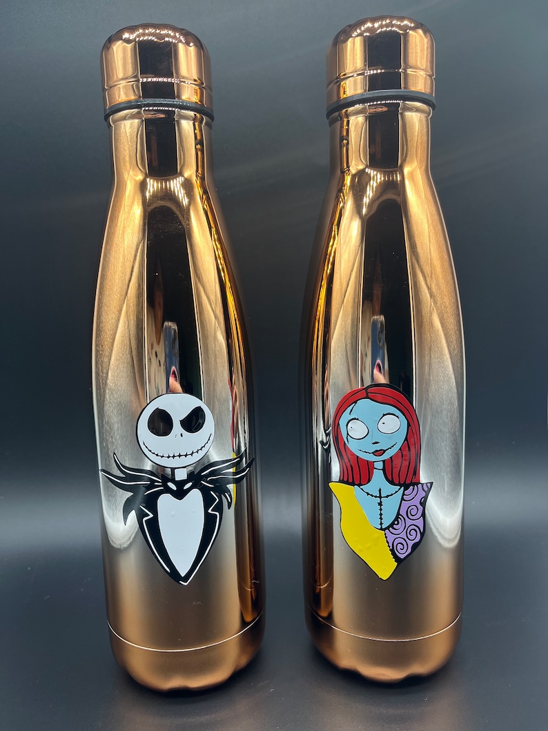 Op de afbeelding: Twee roestvrijstalen waterflessen in ros&eacute;-goud met een Nightmare Before Christmas-thema. De ene fles heeft Jack Skellington en de andere Sally.
