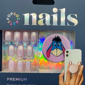 May include: A set of 30 ready-to-wear press-on nails with a pink glitter finish. The set includes a pink PopGrip with a cartoon image of Eeyore from Winnie the Pooh.