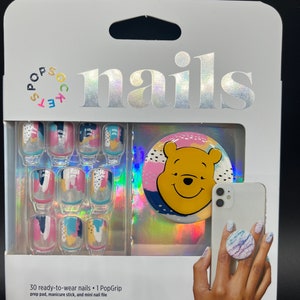 May include: A set of 30 ready-to-wear press-on nails with a Winnie the Pooh themed PopGrip. The nails feature a colorful abstract design with pink, blue, and yellow accents. The PopGrip is a phone accessory that allows you to securely hold your phone.