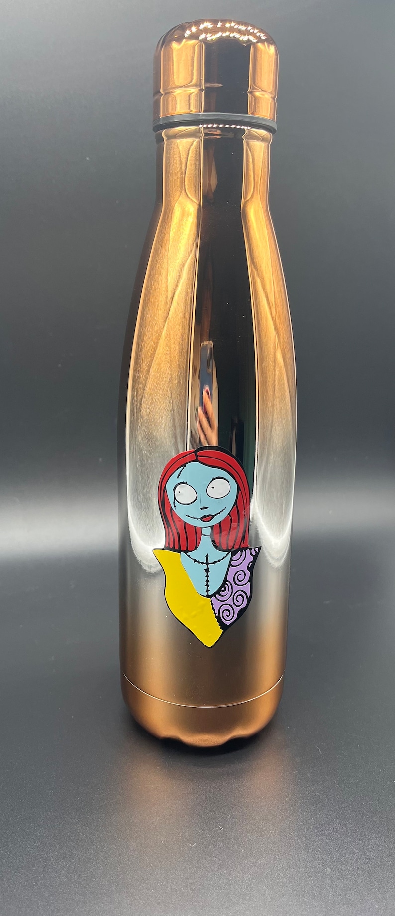 Op de afbeelding: Een koperkleurige waterfles van roestvrij staal met een afbeelding van Sally uit The Nightmare Before Christmas. De afbeelding is in zwart, wit, rood, geel en paars.