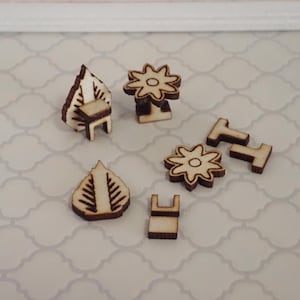 May include: A collection of small, unfinished wooden shapes, including leaf-like forms, flower-like designs, and miniature furniture pieces. The pieces are light brown with darker brown etched details, suggesting a craft or DIY project.