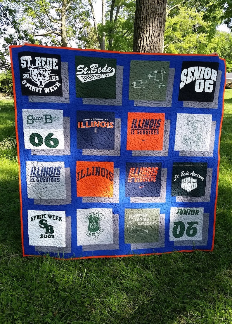 May include: A handmade quilt featuring squares of t-shirts with various logos and text. The quilt has a blue background with orange trim. Some shirts say "St. Bede Spirit Week", "Illinois", and "Senior 06".