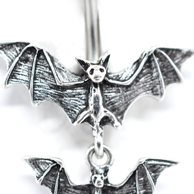 May include: Silver belly button ring with two dangling bats. The bats have detailed wings and faces.