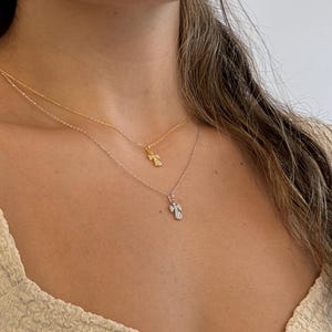 May include: Two delicate necklaces with angel pendants. One necklace is gold, the other is silver. The angel pendants are small and detailed, with a sparkling appearance. The necklaces are layered, creating a stylish and elegant look.