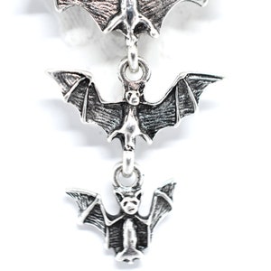 May include: Silver dangle earrings with three bat charms hanging from each other. The bats are detailed and have a textured finish.