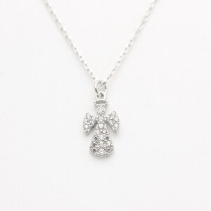 May include: A silver-colored angel pendant necklace. The angel pendant is encrusted with small, clear gemstones. The necklace chain is delicate and silver. The background is plain white.