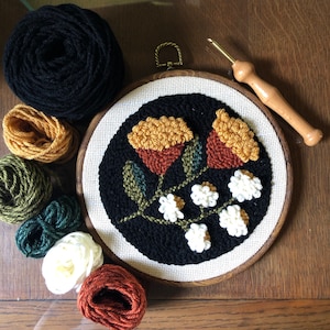 May include: A close-up of a needlepoint embroidery hoop with a floral design. The design features two large yellow and orange flowers with white accents and green leaves. The hoop is surrounded by various colors of embroidery floss.
