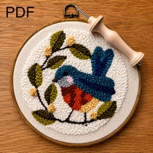 May include: A finished punch needle embroidery featuring a colourful bird design, set within a wooden hoop. The bird is blue, red, and yellow, with green leaves and yellow berries. A punch needle tool rests on the embroidery. The word "PDF" is visible.