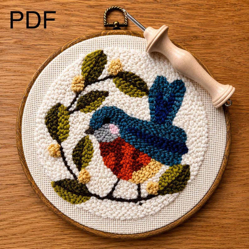 May include: A finished punch needle embroidery featuring a colourful bird design, set within a wooden hoop. The bird is blue, red, and yellow, with green leaves and yellow berries. A punch needle tool rests on the embroidery. The word "PDF" is visible.