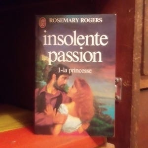 Peut inclure: Un livre de poche intitulé "Insolente Passion" de Rosemary Rogers. La couverture du livre présente un couple en train de s'embrasser, la femme portant une robe blanche et l'homme portant une chemise sombre. Le livre fait partie d'une série intitulée "La Princesse".