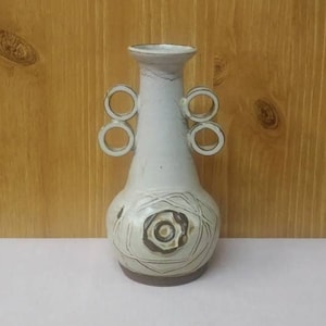 Peut inclure: Un ensemble de trois mugs en céramique avec un glaçage moucheté de couleur crème. Chaque mug présente un motif floral peint à la main différent dans des tons de rose, d'orange et de vert. Les mugs ont une forme simple et arrondie.