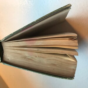 May include: A green hardcover book with the pages fanned out. The book is old and the pages are yellowed.