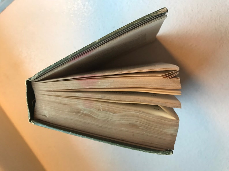 May include: A green hardcover book with the pages fanned out. The book is old and the pages are yellowed.