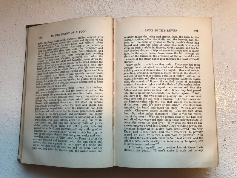 May include: An open book with a cream-colored cover and black text. The text on the left page reads "In the Heart of a Fool" and the text on the right page reads "Love is the Lever".