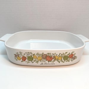 Op de afbeelding: Witte rechthoekige ovenschaal met een kleurrijk fruit- en bloemmotief. De schaal heeft twee handvatten en de woorden "Le Romarin" staan op de voorkant. Het ontwerp omvat citroenen, tomaten en andere producten.