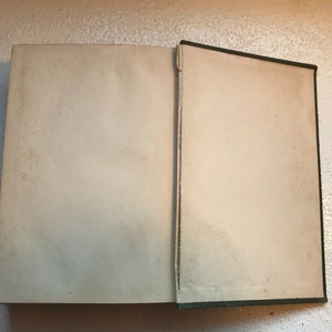 May include: An open book with a green cover and blank white pages. The book is lying flat on a white surface.