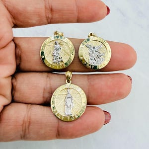 May include: Three gold-tone religious pendants with detailed figures and the inscription "PRAY FOR US" in a circular design. The pendants feature Saint Michael, Saint Barbara, and another saint.