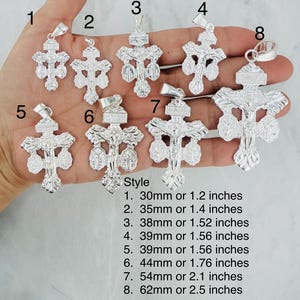 Puede incluir: Una colección de colgantes de crucifijo plateados, cada uno con una detallada representación de Jesucristo. Los colgantes varían en tamaño, desde 30 mm hasta 62 mm de longitud. Cada colgante tiene un lazo para sujetarlo a una cadena.