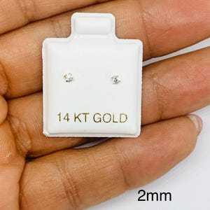 May include: A pair of small, round, clear stud earrings on a white card with the text "14 KT GOLD" and "2mm".