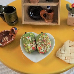 May include: A miniature Mexican-themed table setting with a yellow table, a small wooden shelf with pottery, a cactus, a woven basket, a small bowl with green pears, and a brown clay mug.