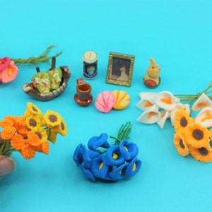 May include: Assortment of miniature artificial flower bouquets in various colors, including orange, yellow, white, blue, and pink. The bouquets are arranged on a blue surface with other miniature items, such as a small picture frame, a ceramic mug, and a small ceramic bowl.