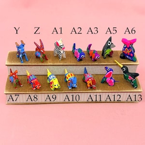 K&ouml;nnte beinhalten: Eine Sammlung kleiner, handbemalter Tierfiguren, die auf zwei abgestuften Holzregalen angeordnet sind. Die Figuren sind mit Y, Z, A1, A2, A3, A5, A6, A7, A8, A9, A10, A11, A12 und A13 beschriftet und weisen lebendige, bunte Muster auf.