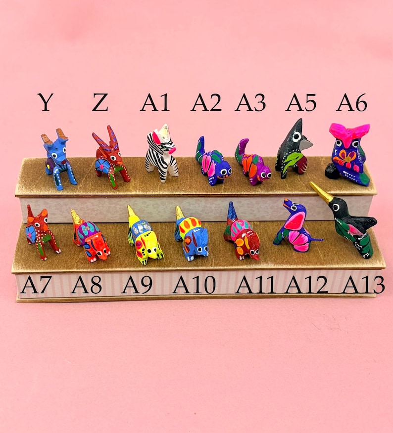 K&ouml;nnte beinhalten: Eine Sammlung kleiner, handbemalter Tierfiguren, die auf zwei abgestuften Holzregalen angeordnet sind. Die Figuren sind mit Y, Z, A1, A2, A3, A5, A6, A7, A8, A9, A10, A11, A12 und A13 beschriftet und weisen lebendige, bunte Muster auf.
