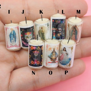 May include: A collection of eight miniature cylindrical candles labeled I through P, each featuring a unique religious or cultural graphic print. The candles are white with a single black wick and are arranged in a group, displaying various icons.