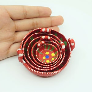 May include: Set of five red nesting bowls with white polka dots and green and yellow painted designs. The bowls are hand-painted and have a rustic look.