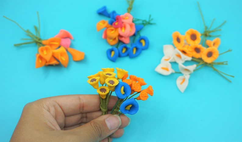 May include: Assortment of artificial flower bouquets in various colors, including yellow, orange, blue, white, and pink. The flowers are made of polymer clay and have a realistic appearance.