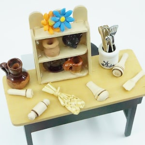 May include: A miniature wooden table with a shelf unit, a brown pitcher, a rolling pin, a whisk, and a utensil holder with a windmill design. The shelf unit has a blue and orange flower on top and holds small brown pottery items.