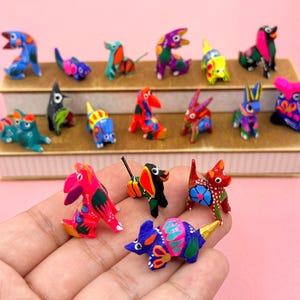 K&ouml;nnte beinhalten: Eine Sammlung kleiner, handbemalter Tierfiguren aus Holz mit lebendigen, mehrfarbigen Mustern. Die Figuren stellen verschiedene Tiere wie Hunde, Katzen und V&ouml;gel dar und sind auf einem gestuften St&auml;nder sowie in einer Handfl&auml;che zu sehen.