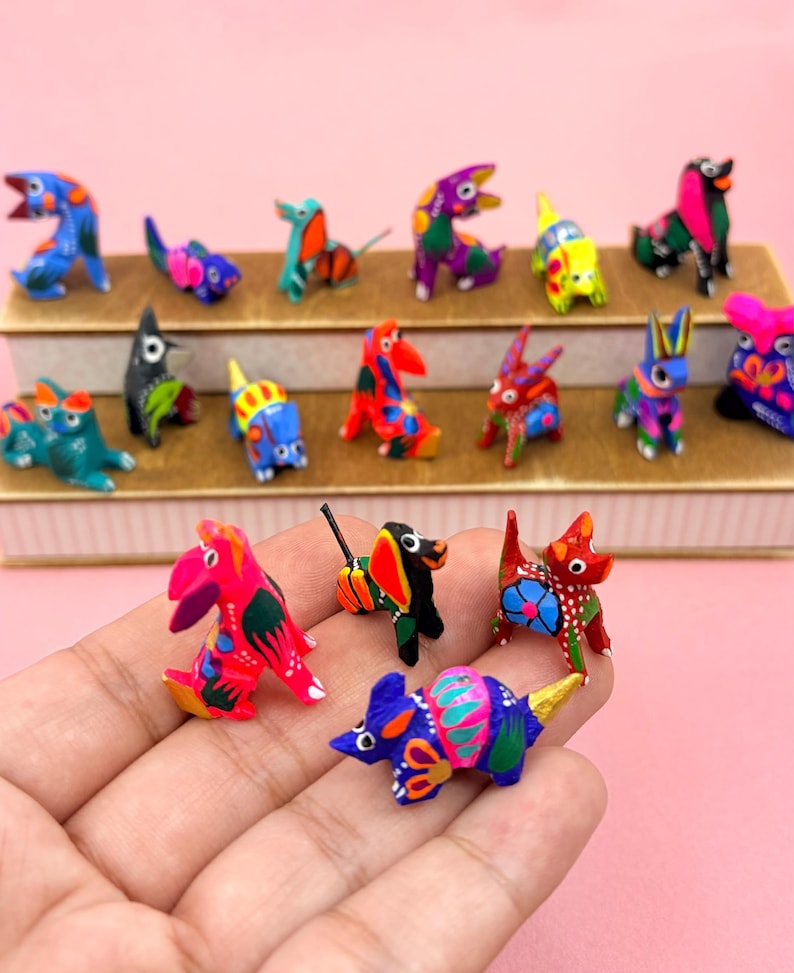 K&ouml;nnte beinhalten: Eine Sammlung kleiner, handbemalter Tierfiguren aus Holz mit lebendigen, mehrfarbigen Mustern. Die Figuren stellen verschiedene Tiere wie Hunde, Katzen und V&ouml;gel dar und sind auf einem gestuften St&auml;nder sowie in einer Handfl&auml;che zu sehen.