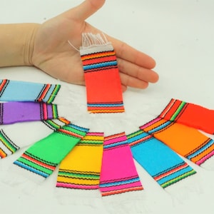 May include: A set of ten miniature colorful woven blankets with white fringe. The blankets are arranged in a circle with a hand holding one in the center.