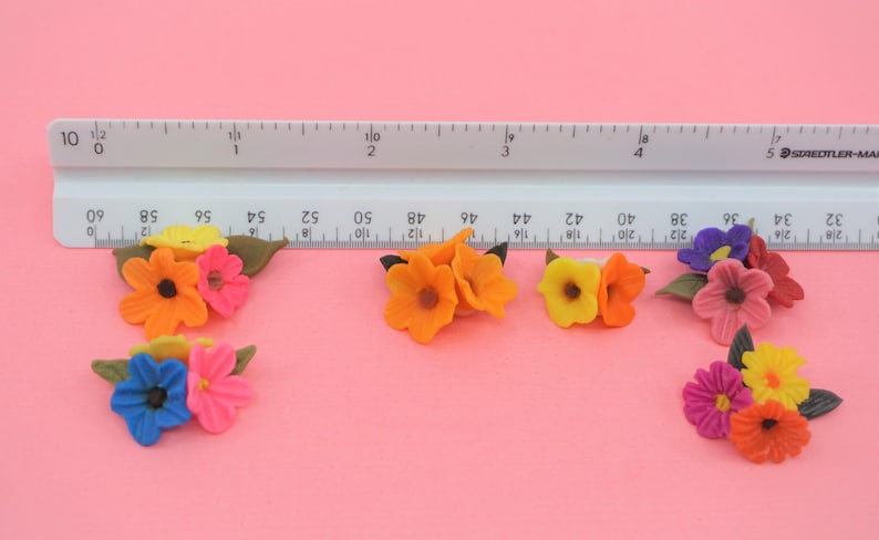 Pode incluir: Uma cole&ccedil;&atilde;o de flores de feltro coloridas em tons de laranja, rosa, amarelo, azul e roxo. As flores est&atilde;o dispostas em pequenos grupos, cada um com folhas de feltro verde. Uma r&eacute;gua &eacute; colocada acima das flores para escala.