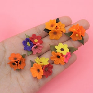 Pode incluir: Um conjunto de cachos de flores em miniatura, coloridos, em tons de laranja, amarelo, vermelho, rosa e roxo. Cada cacho apresenta p&eacute;talas detalhadas e folhas verdes, sobre um fundo rosa suave.