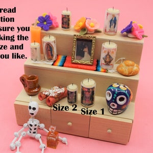 May include: A three-tiered wooden display stand featuring miniature candles with religious imagery, a small framed picture, a colorful woven runner, a bread roll, a brown ceramic mug, a skull figurine, and a white skeleton figure with black spots.