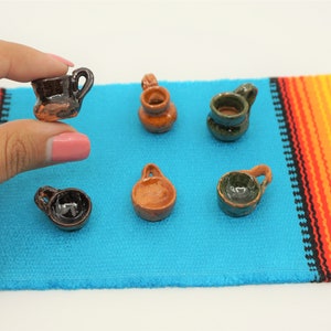 May include: A set of six miniature ceramic cups and bowls in various shades of brown, green, and black. The cups and bowls are arranged on a colorful woven rug.