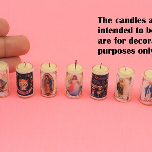 May include: Eight miniature cylindrical candles featuring various religious and cultural imagery, including skulls and figures. The text states: The candles are not intended to be lit. They are for decoration purposes only. Each candle has a small wick.