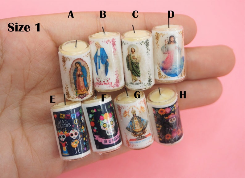 May include: A collection of eight miniature cylindrical candles labeled A through H, featuring religious and cultural imagery including Our Lady of Guadalupe, Virgin Mary, Saint Jude, Jesus, and Dia de los Muertos sugar skulls with floral accents.