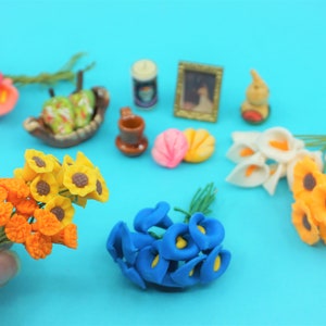 May include: A collection of miniature artificial flowers in various colors, including yellow, orange, blue, and white. The flowers are arranged in bouquets and are displayed on a blue surface.