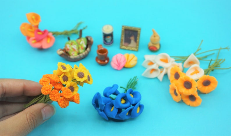 May include: A collection of miniature artificial flowers in various colors, including yellow, orange, blue, and white. The flowers are arranged in bouquets and are displayed on a blue surface.
