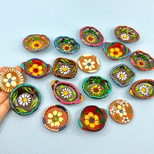 Könnte beinhalten: Eine Sammlung von 16 kleinen, bunten Keramikschalen mit Blumendesigns. Die Schalen sind handbemalt mit leuchtenden Farben und filigranen Mustern. Sie eignen sich perfekt zum Servieren von kleinen Snacks oder Dips.