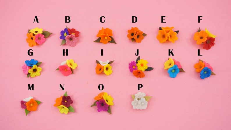 Pode incluir: Uma cole&ccedil;&atilde;o de arranjos florais de feltro coloridos, cada um com uma combina&ccedil;&atilde;o &uacute;nica de tons como laranja, rosa, amarelo e azul. As flores s&atilde;o dispostas em pequenos grupos, com folhas de feltro verde, sobre um fundo rosa.
