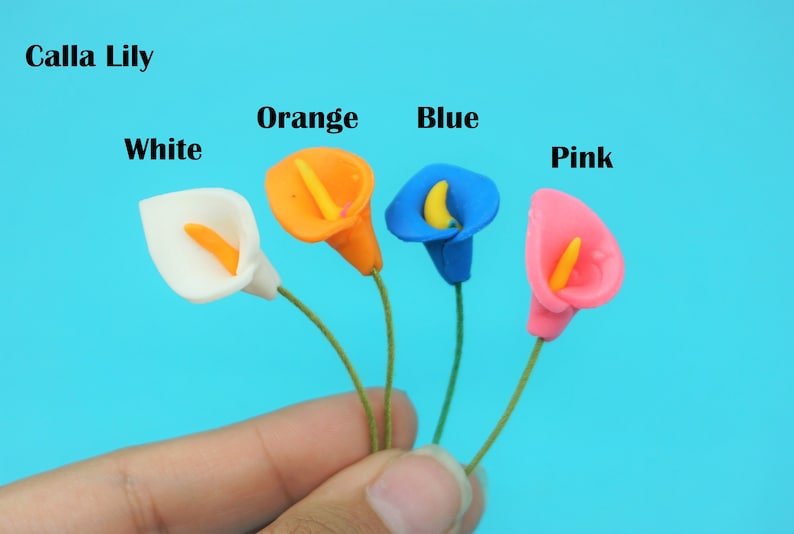 May include: Five artificial Calla Lily flowers in white, orange, blue, and pink. The flowers are held in a hand against a blue background.