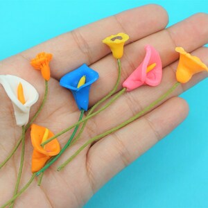 May include: A set of seven artificial calla lily flowers in various colors, including white, orange, yellow, pink, and blue. The flowers are made of a soft, pliable material and have a realistic appearance.