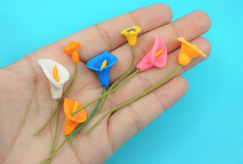 May include: A set of seven artificial calla lily flowers in various colors, including white, orange, yellow, pink, and blue. The flowers are made of a soft, pliable material and have a realistic appearance.