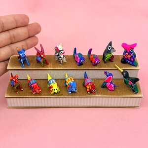 K&ouml;nnte beinhalten: Eine Sammlung von vierzehn kleinen, handbemalten Tierfiguren aus Holz, die auf einem zweistufigen St&auml;nder angeordnet sind. Die Miniaturfiguren weisen lebendige, mehrfarbige Muster auf, darunter Streifen, Punkte und florale Motive.